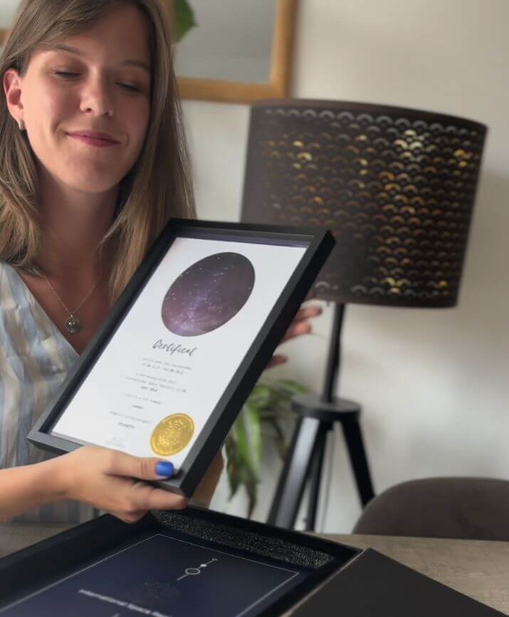 Une femme tient un certificat encadré au-dessus d’un coffret cadeau ouvert.