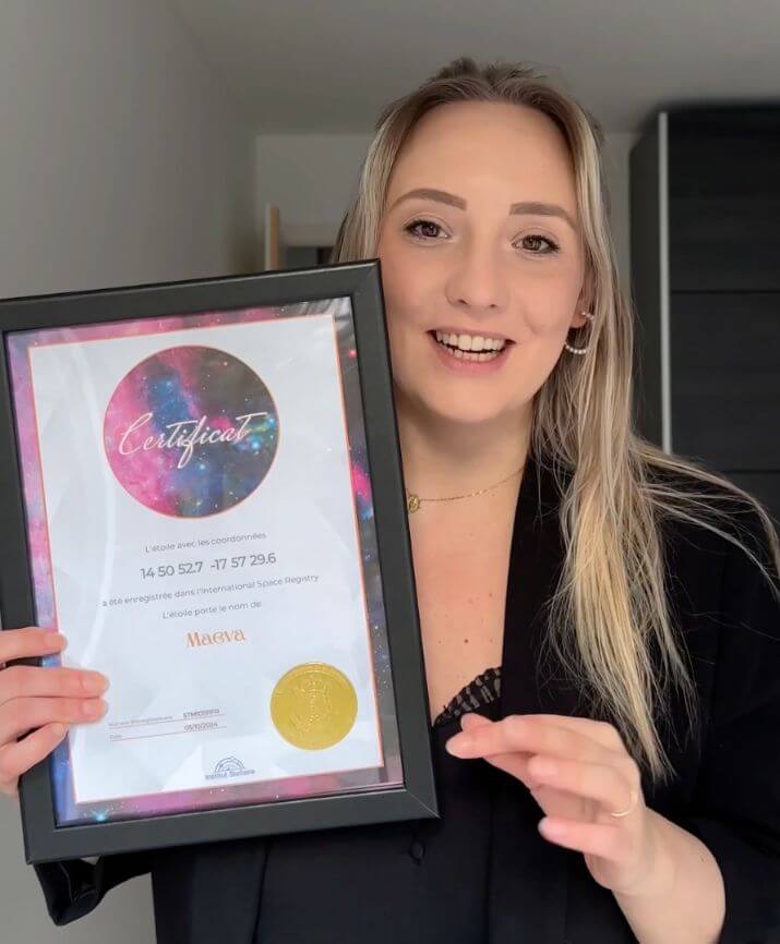 Une femme souriante présente un certificat d’étoile au motif rose dans un cadre noir.